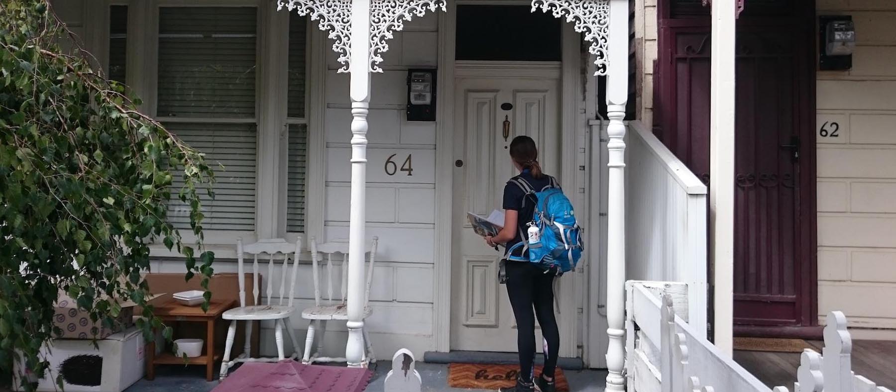 Woman standing outside at the front door of a terrace house with a clipboard